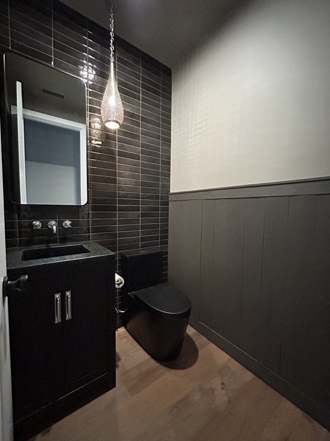 Powder room with dark tile, wall-mounted faucet, and pendant lighting