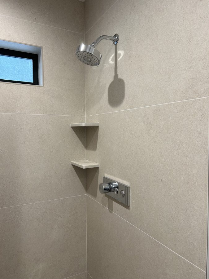 Tiled shower with chrome showerhead and corner shelves