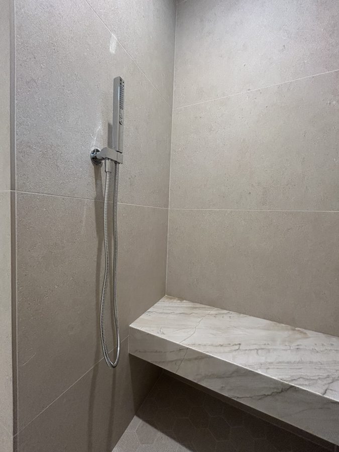 Tiled shower with handheld fixture and a stone bench