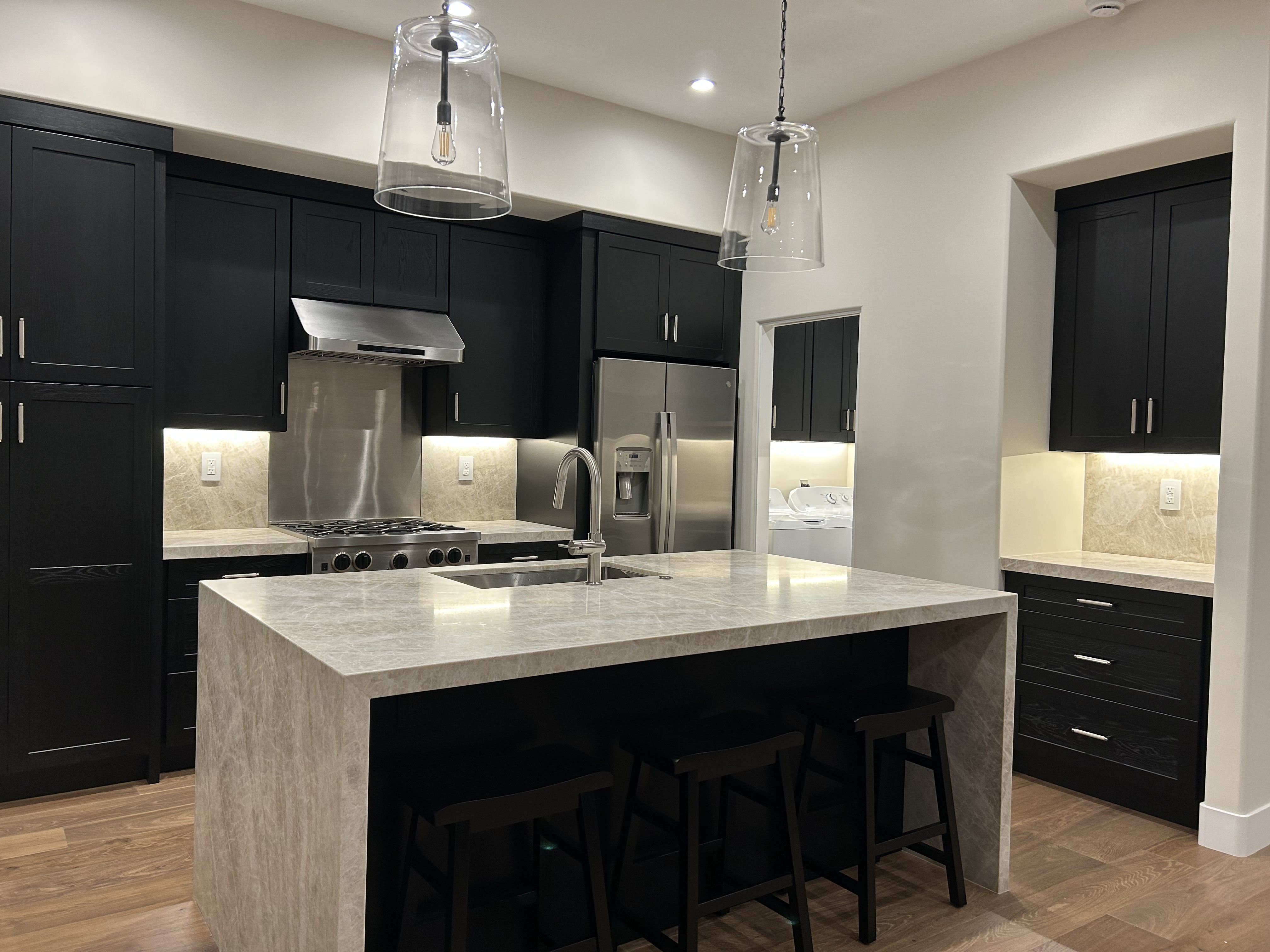 Kitchen with dark cabinetry, a stone waterfall island, stainless steel appliances, and glass pendant lights